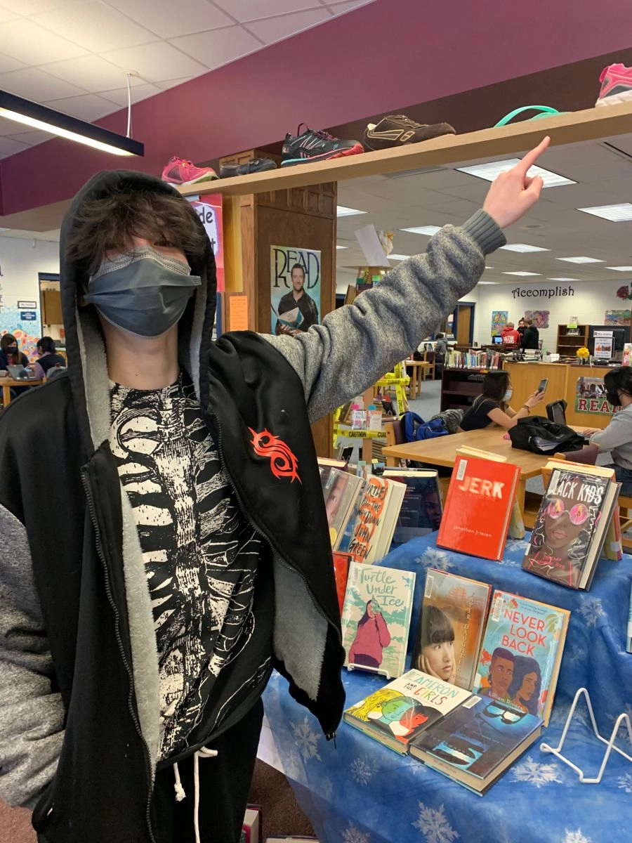 A man wearing a mask standing in front of a book shelf.