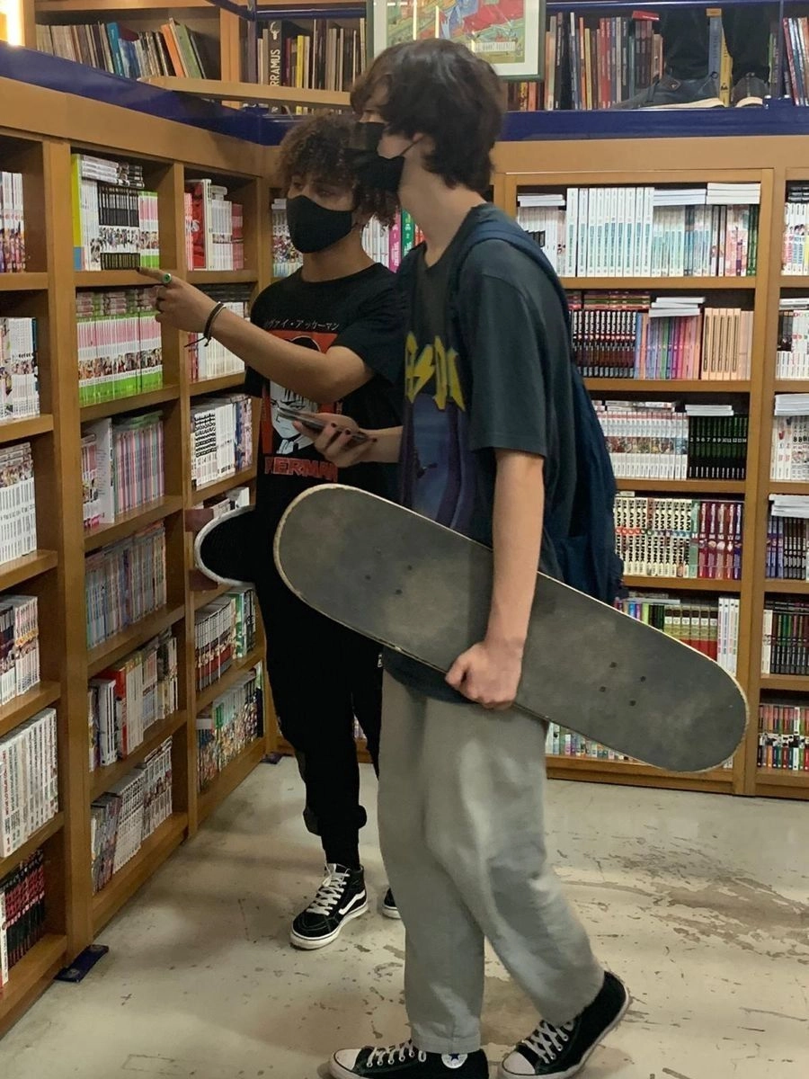 A group of people standing in front of a book shelf holding a skateboard.