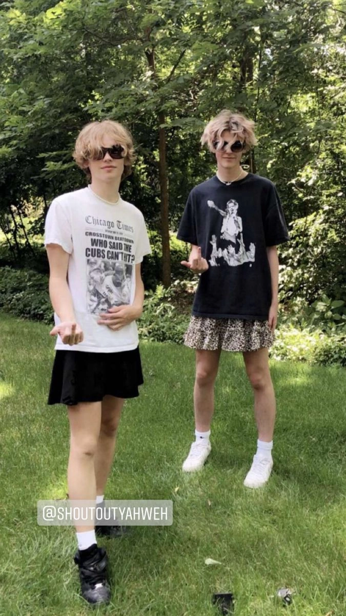 two young men standing next to each other in front of a hedge