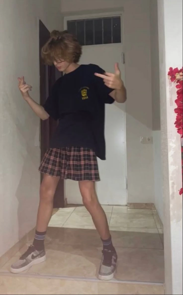 A woman in a black shirt and plaid skirt standing in front of a door.