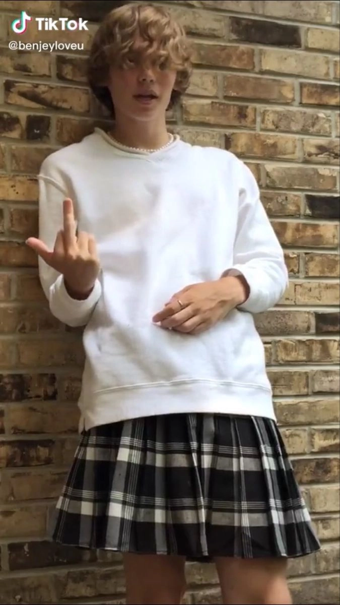 A woman in a white sweatshirt and plaid skirt posing for a picture.