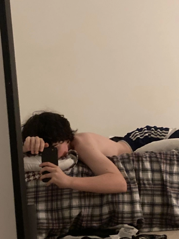 A man laying on top of a bed looking at his cell phone.