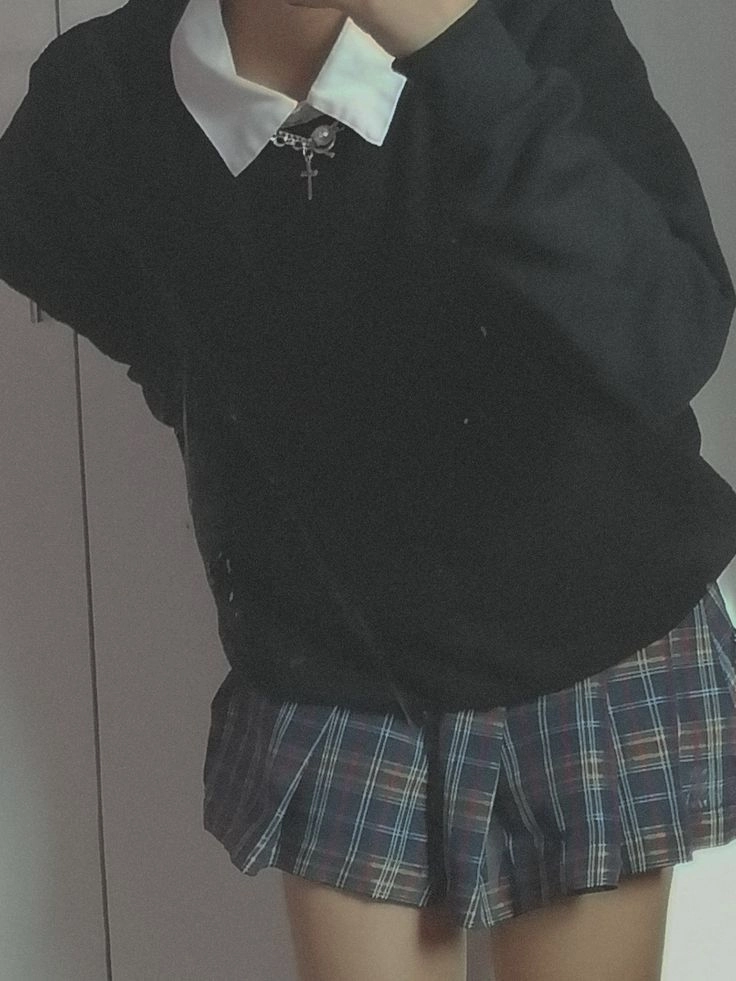 A woman in a black shirt and plaid skirt is taking a selfie.