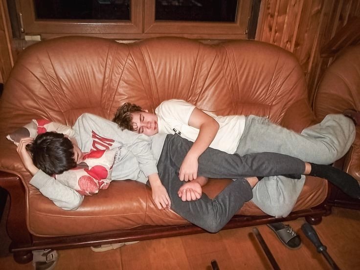 A group of people laying on top of a brown couch.