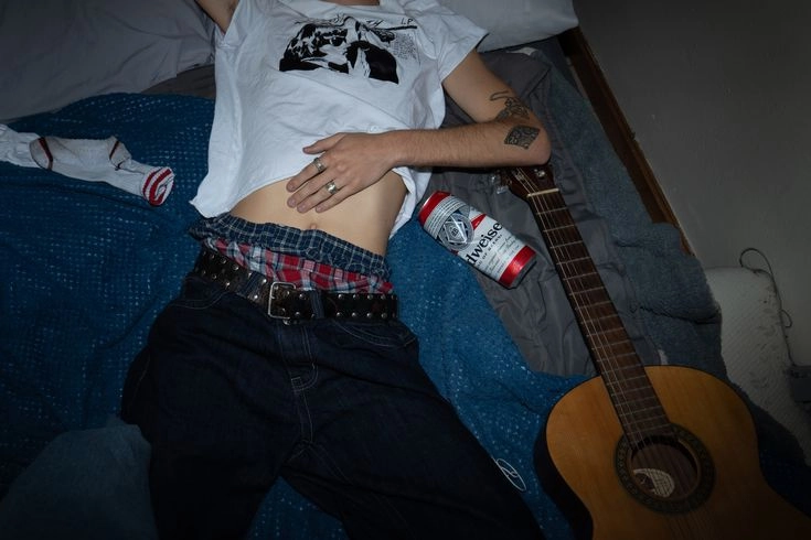 A woman laying on a bed with a guitar and a can of beer.