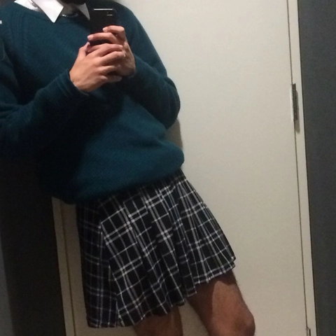 A man in a blue sweater and a black and white plaid skirt.
