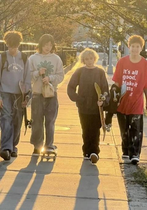 A group of people walking down a sidewalk with skateboards.