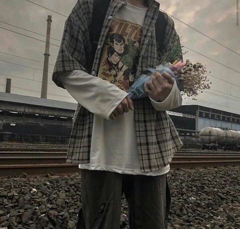 A man standing on a train track holding a bunch of flowers.