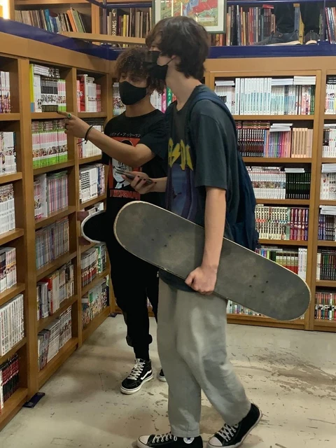 A group of people standing in front of a book shelf holding a skateboard.