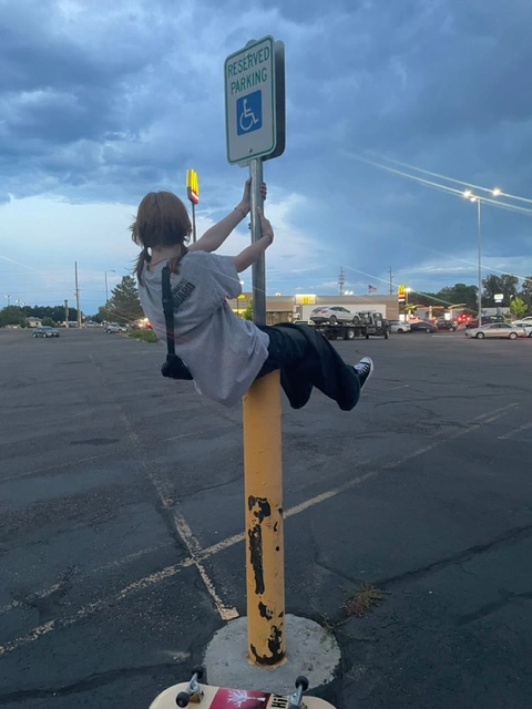 A person sitting on top of a pole in a parking lot.