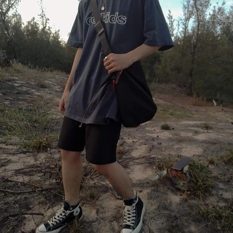 A man in a black shirt and black shorts standing in the woods.