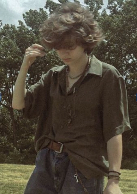 A young man with curly hair standing in a field.