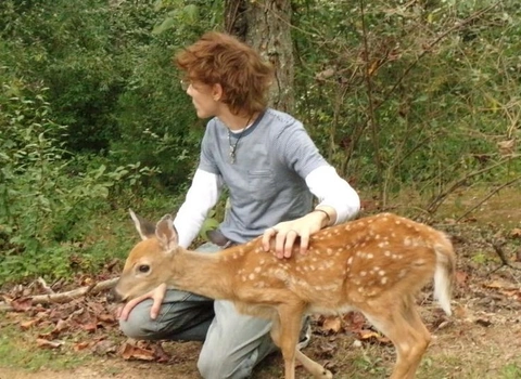 A woman kneeling down next to a deer in the woods.