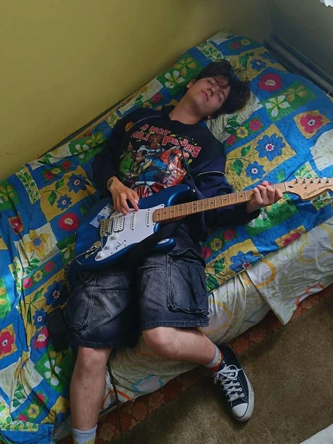 A man laying on top of a bed playing a guitar.