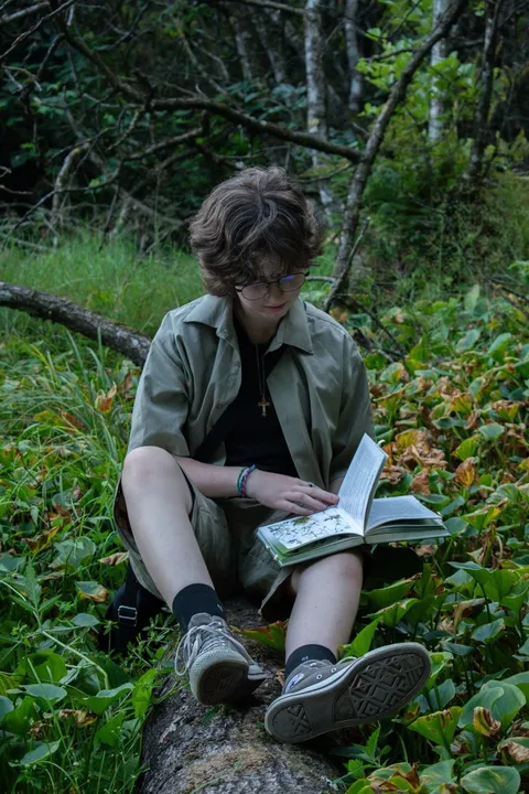 A woman sitting on a rock reading a book.