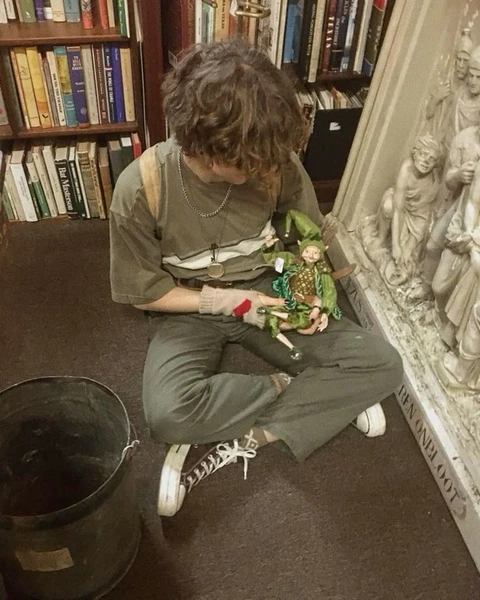A woman sitting on the floor in front of a book shelf.