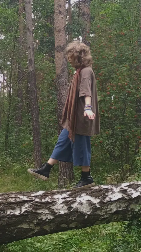 A woman walking through a forest with a scarf around her neck.