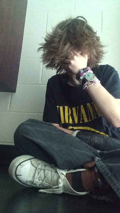 A young man with curly hair sitting on the floor.