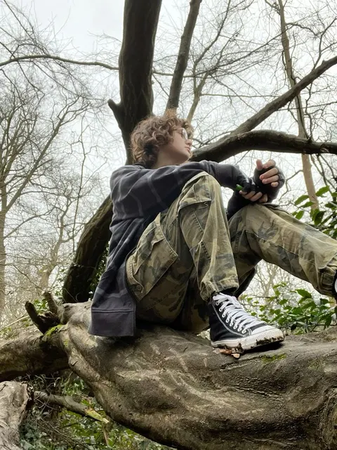 A man sitting on top of a tree branch in the woods.