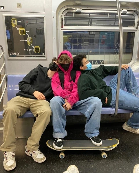 A group of people sitting on a subway train with skateboards.