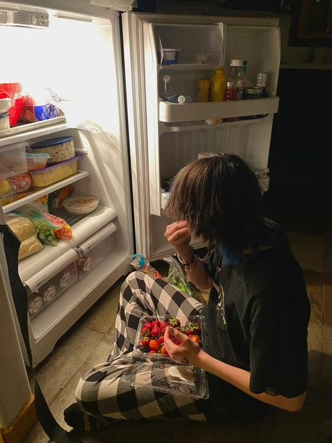 A woman sitting in front of an open refrigerator.