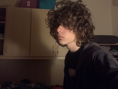A young man with curly hair standing in a kitchen.