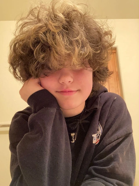 A young boy with curly hair is posing for a picture.