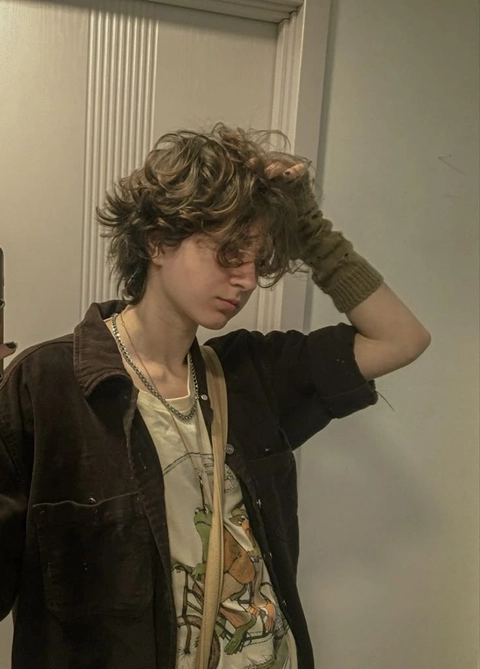 A young man with curly hair standing in front of a mirror.