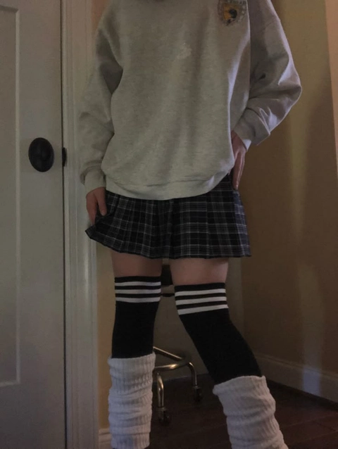 A woman in a gray sweatshirt and plaid skirt with knee high socks.