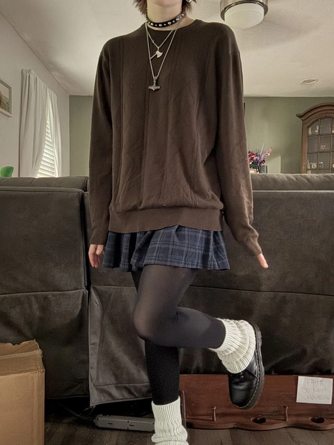 A woman in a brown sweater and plaid skirt is posing for a picture.