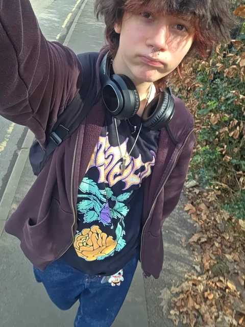 A young man wearing headphones standing in front of a fence.