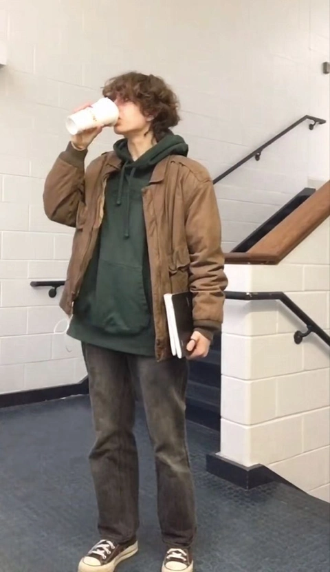 A man standing in front of a stairwell drinking from a cup.