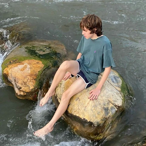 A young boy sitting on a rock in the water.
