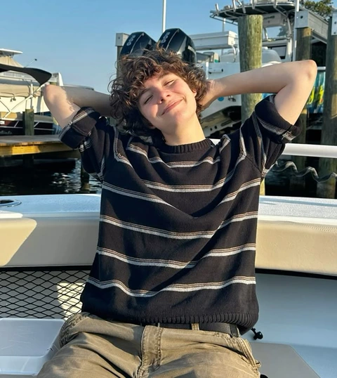 A young boy sitting on top of a boat with his arms outstretched.