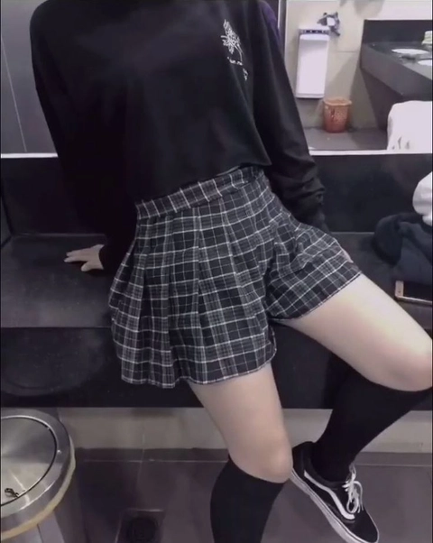A woman in a black shirt and plaid skirt is posing for a picture.