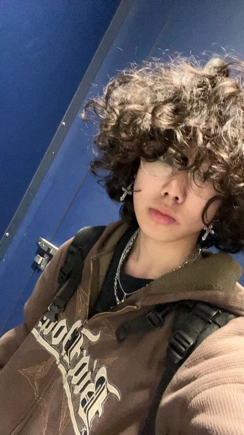 A young boy with curly hair wearing a brown jacket.