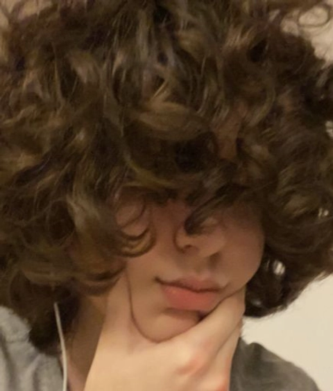 A woman with curly hair is holding her head in her hands.