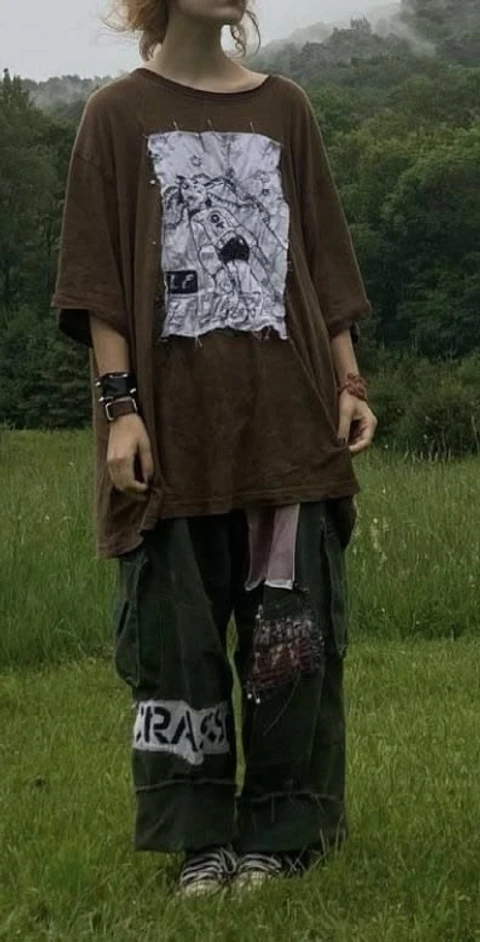 A man standing in a field wearing a brown shirt and green pants.