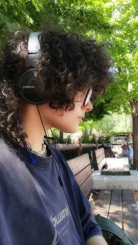 A young man with curly hair sitting on a bench.