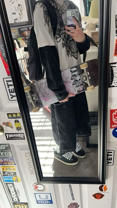 A man holding a skateboard in front of a mirror.