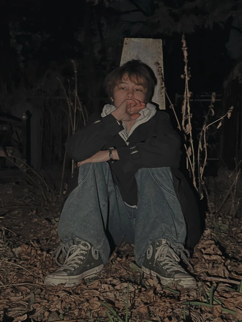 A young boy sitting on the ground in front of a fence.
