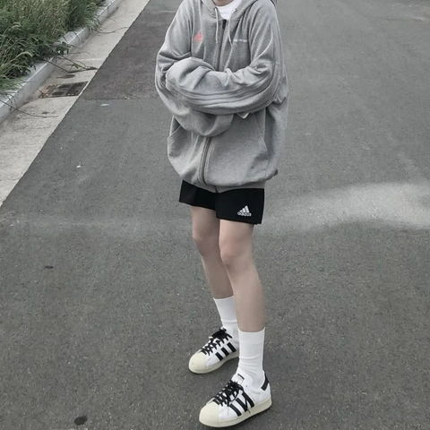 A person wearing a hoodie and black shorts standing on a sidewalk.