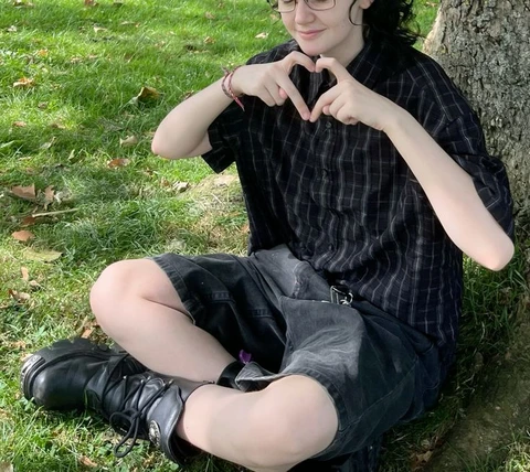 A woman sitting on the ground making a heart with her hands.