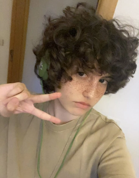 A young boy with curly hair is making a peace sign.