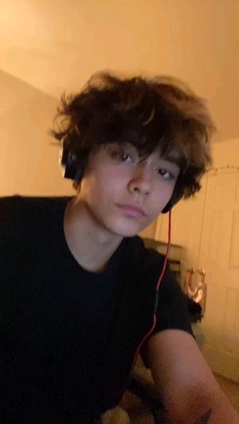 A young man with curly hair is taking a selfie.
