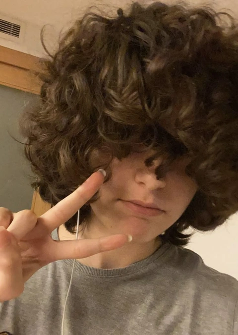 A young boy with curly hair making a peace sign.