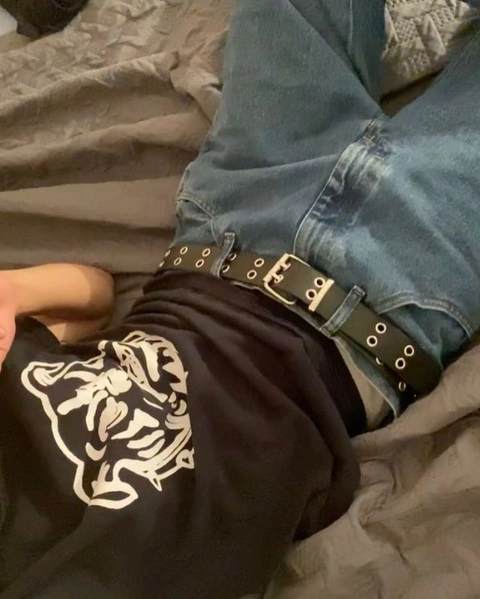 A pair of jeans with a belt on a bed.