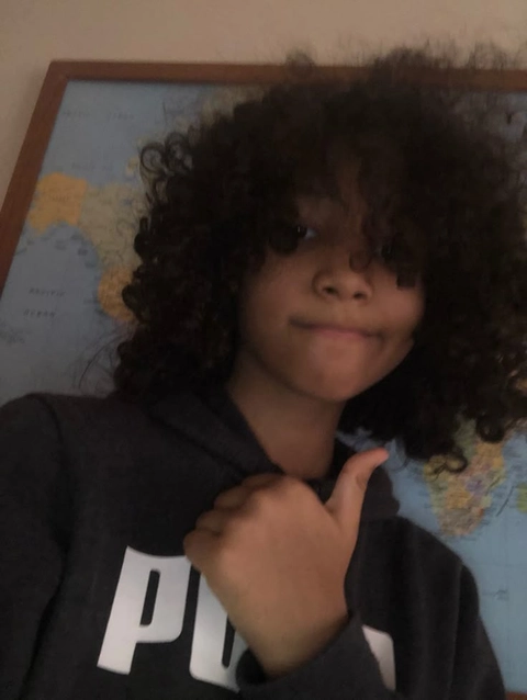 A young boy with curly hair making a peace sign.