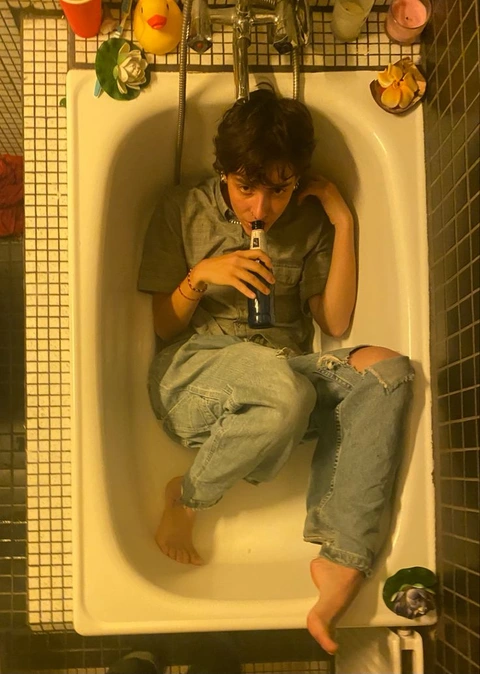 A man sitting on top of a toilet holding a bottle of beer.
