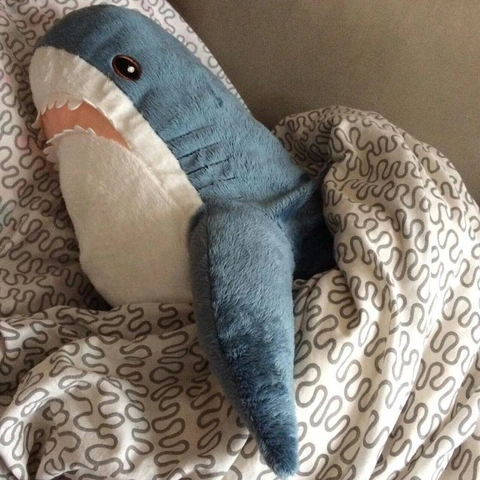 A stuffed shark is laying on a bed.